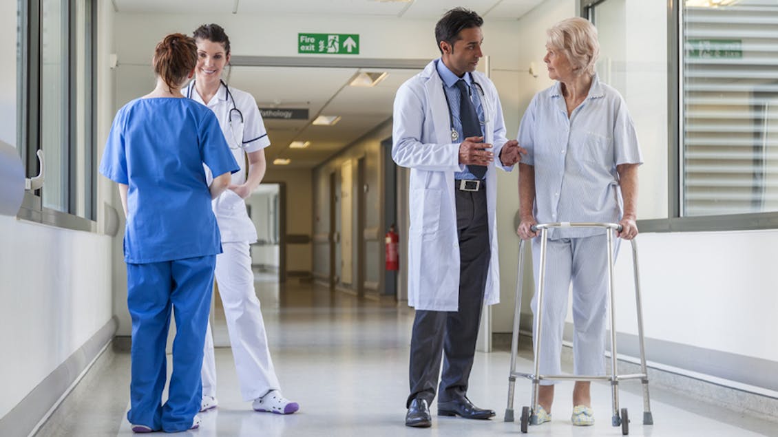 Four people in a hospital hall, on the left two doctors talking to each other and on the right a doctor talking with a patient