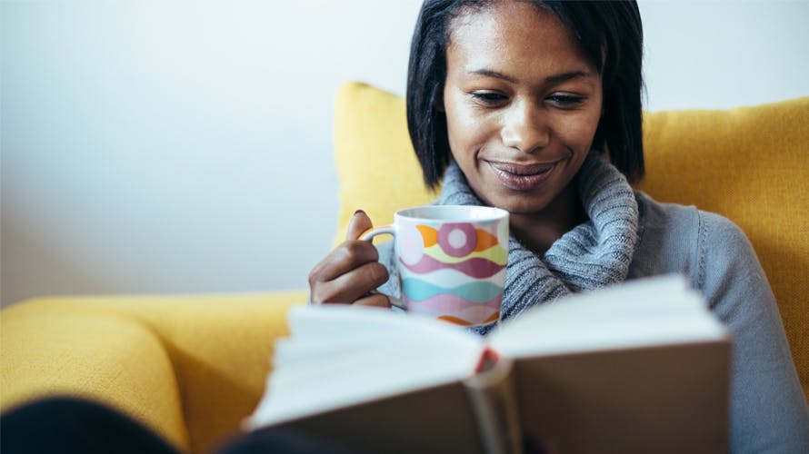 A woman reading a book with a cup of coffee on her hand