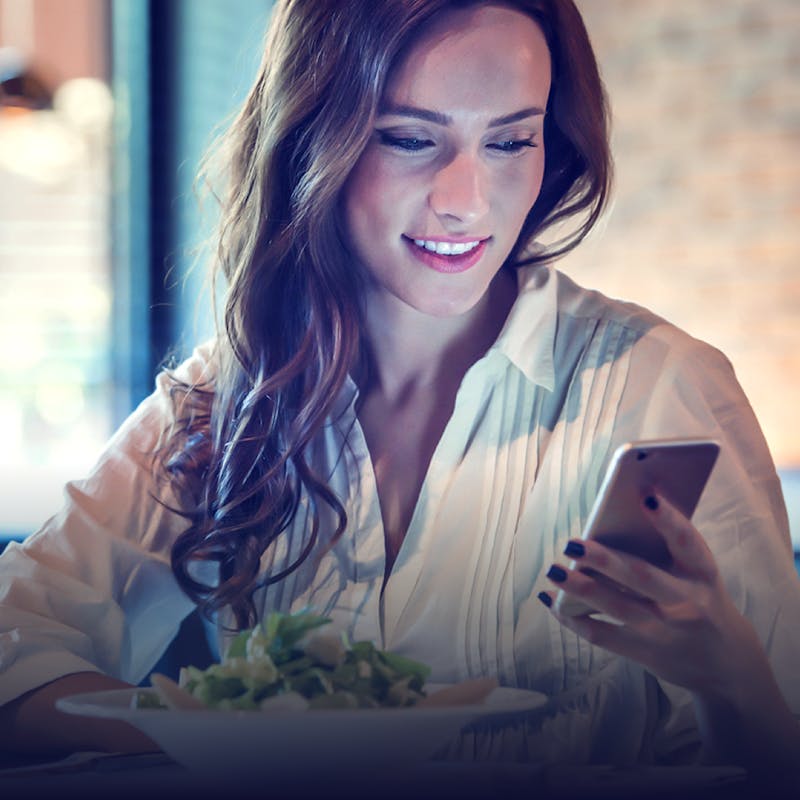 a woman looking at her phone and eating a salad