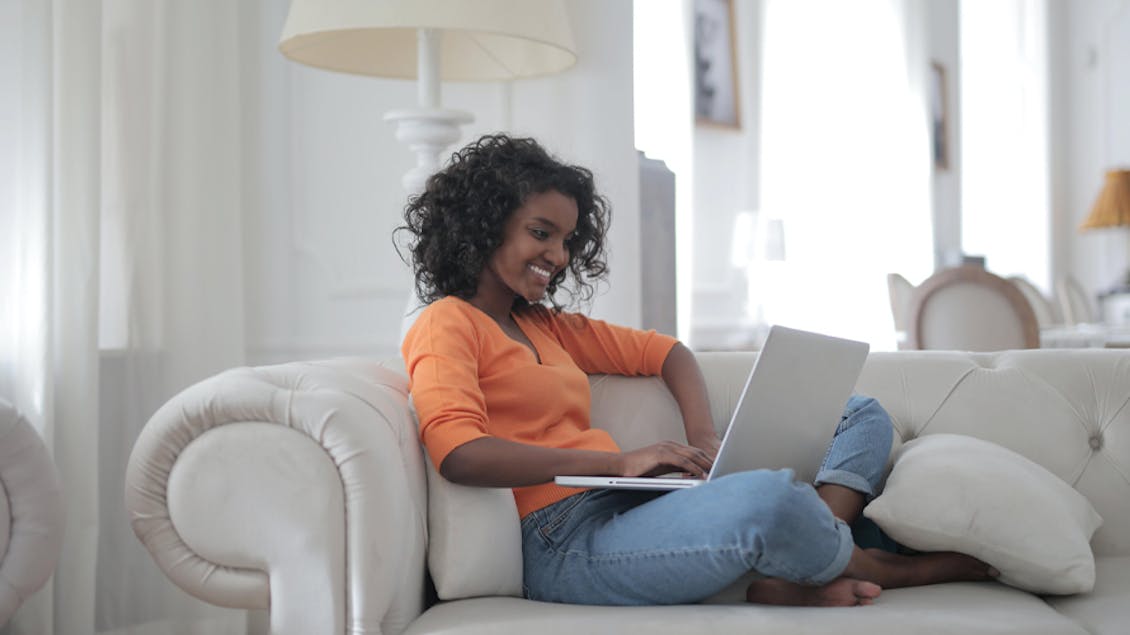 a woman sitting on her couch looking at her computer smilling 