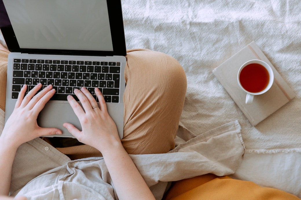 computer on a bed with a cup of tea