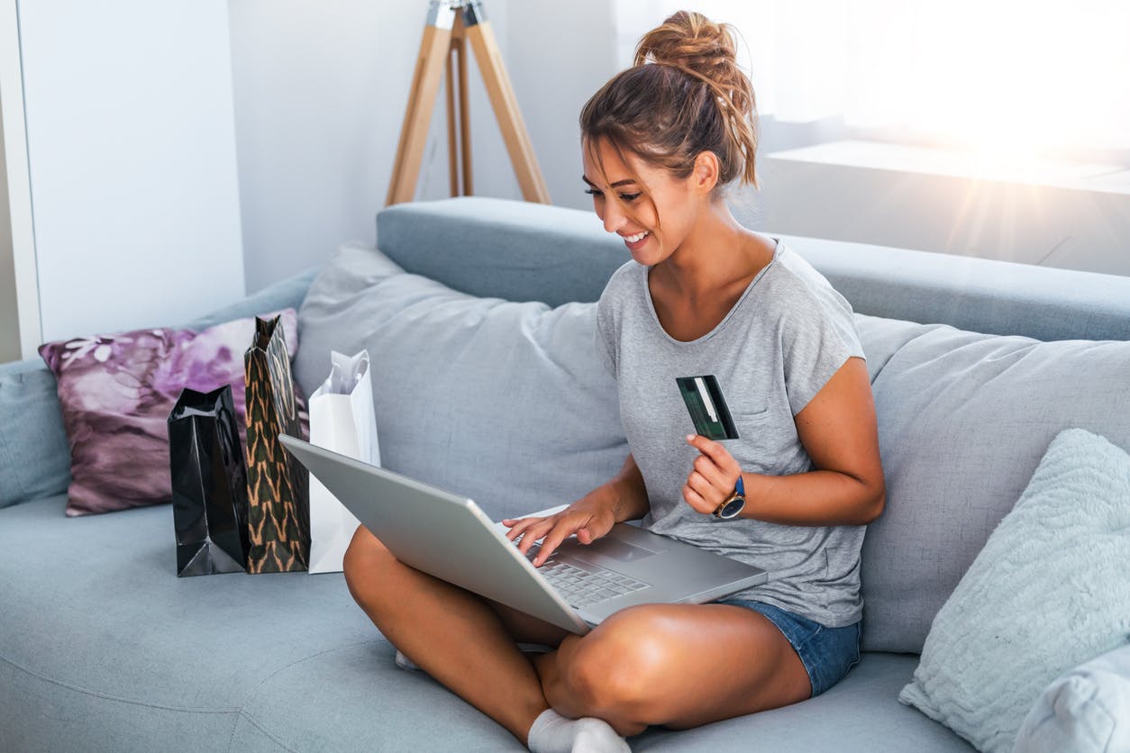 femme assise sur un canapé, carte bleue à la main, avec un ordinateur