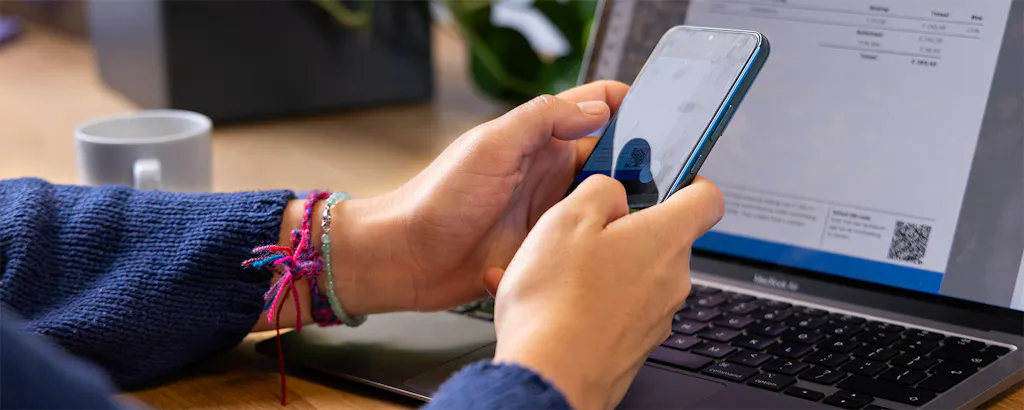 Handen die een qr-code scannen van een laptop scherm om een factuur te betalen