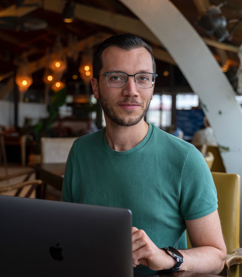 Simon zit achter zijn laptop en kijkt in de camera