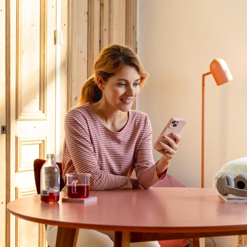 Fysiotherapeut kijkt lachend op telefoon terwijl ze aan tafel zit met een kop thee