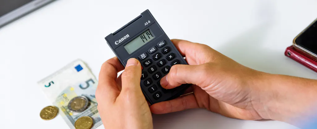 Hand met rekenmachine met geld en briefgeld en muntgeld