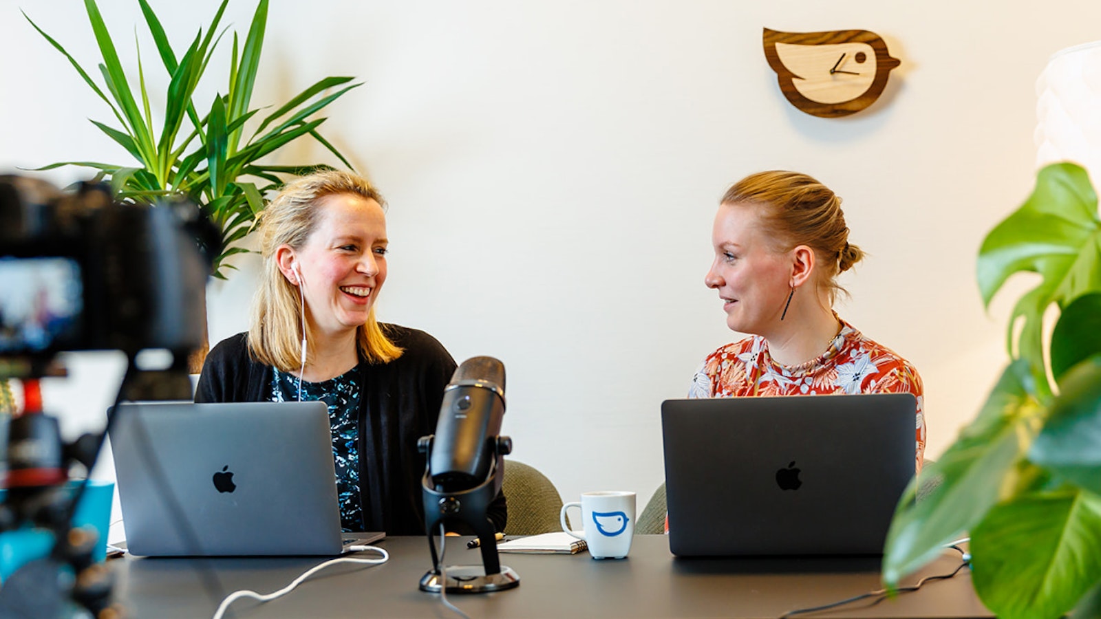 Liesbeth en Loes kijken elkaar lachend aan achter laptops tijdens livesessie