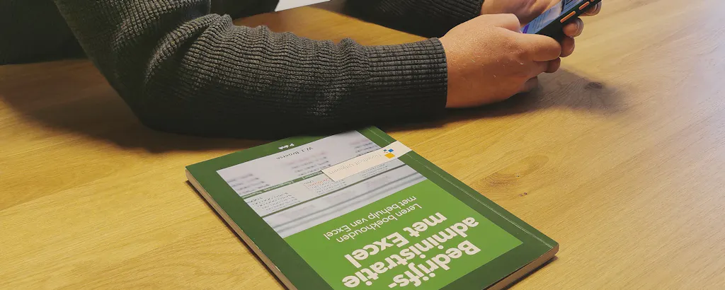 Wietse met zijn telefoon en boek boekhoudcursus Bedrijfsadministratie in Excel
