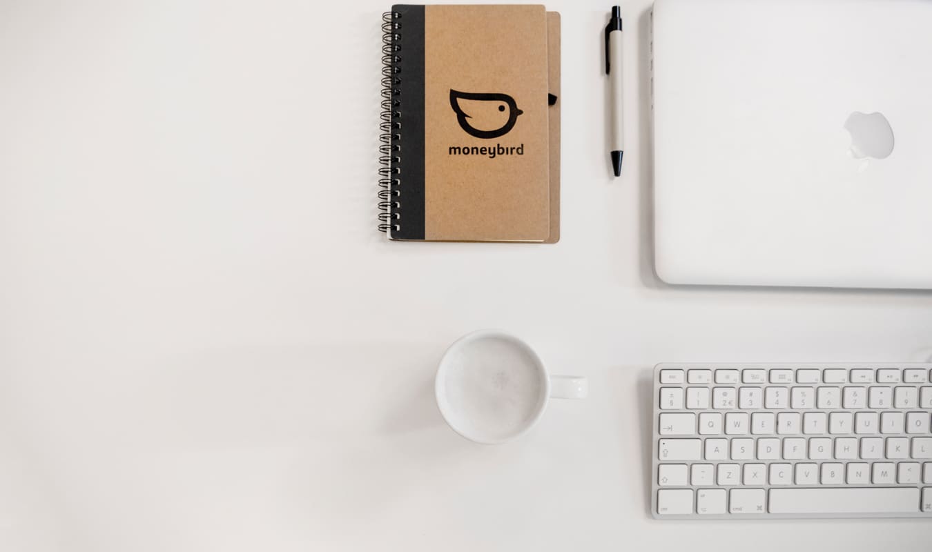 een laptop, kopje, toetsenbord en schrijfblokje