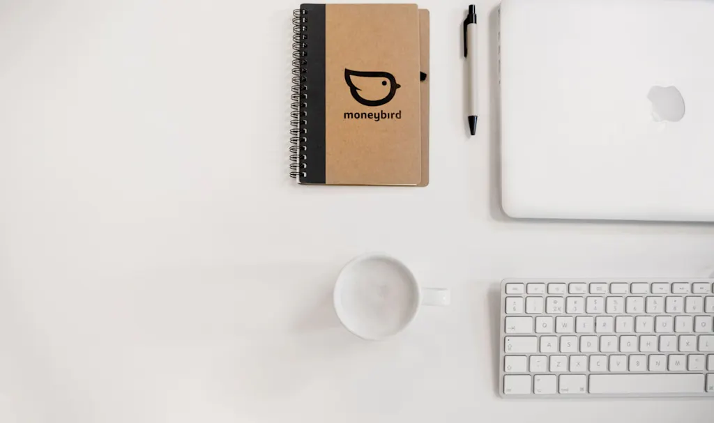 een laptop, kopje, toetsenbord en schrijfblokje