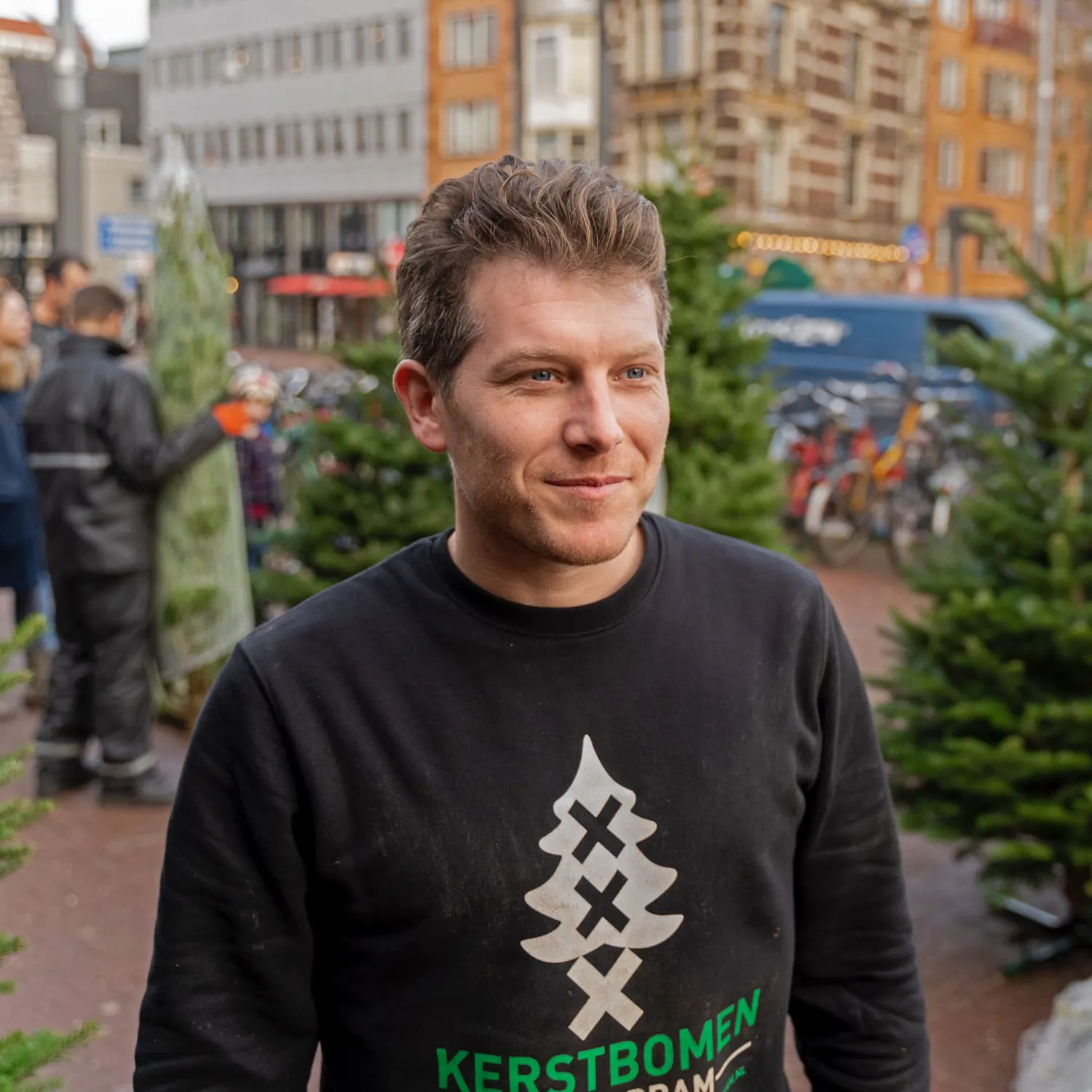 Alex kijkt langs de camera terwijl hij kerstbomen verkoopt