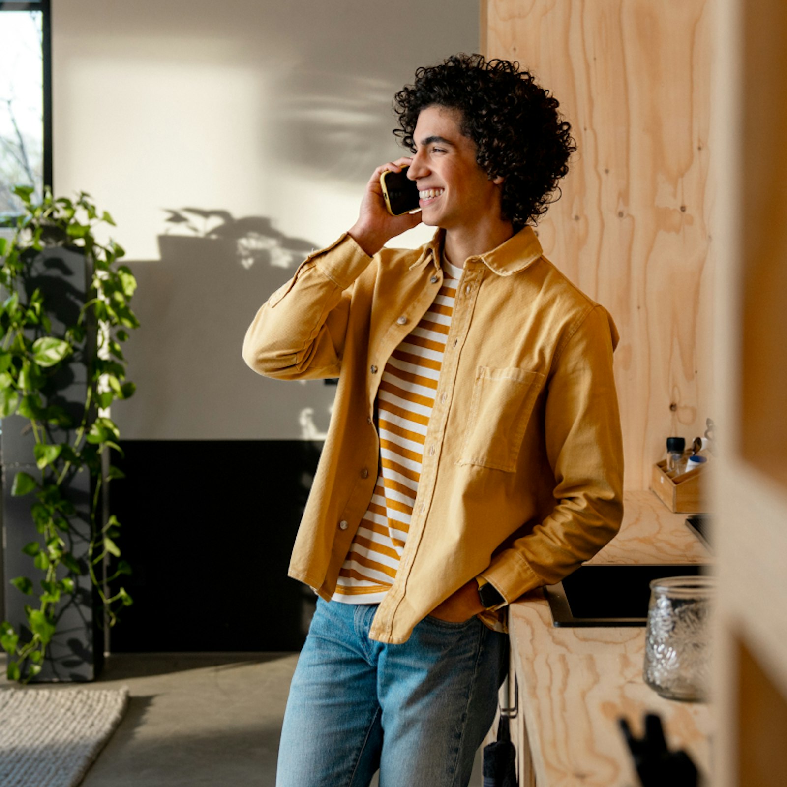 Ondernemer leunt in een keuken tegen het aanrecht terwijl hij lachend aan het bellen is