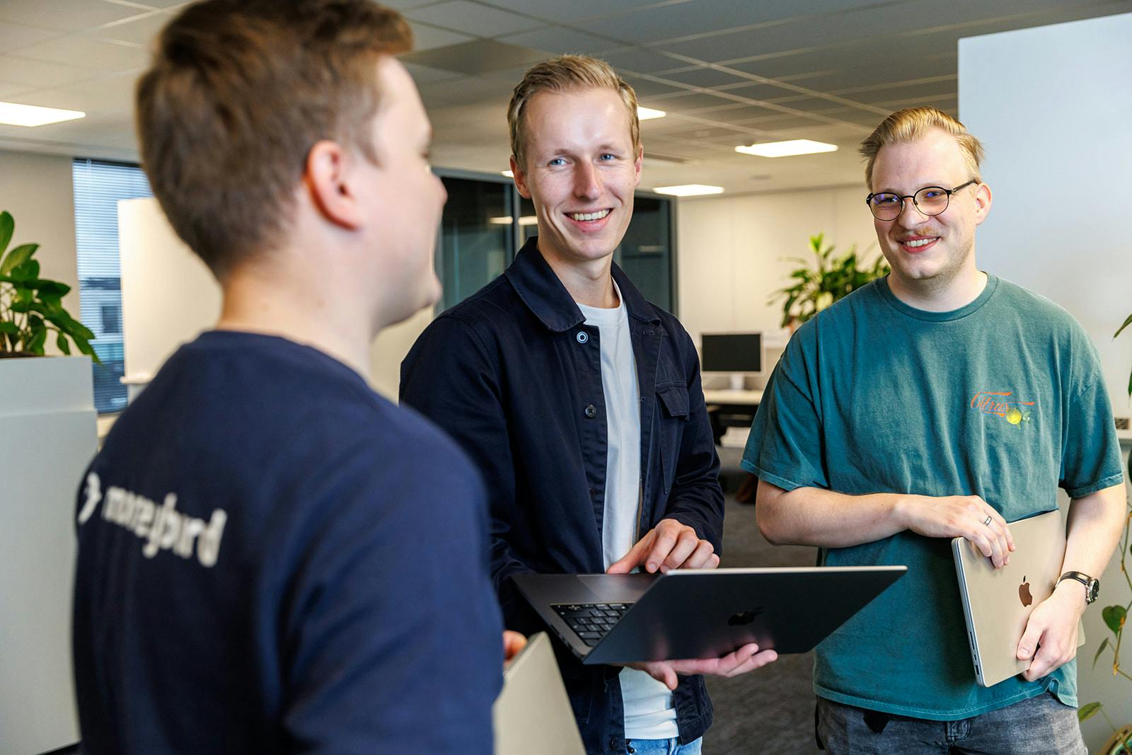 Drie collega'a op de werkvloer lachend in gesprek