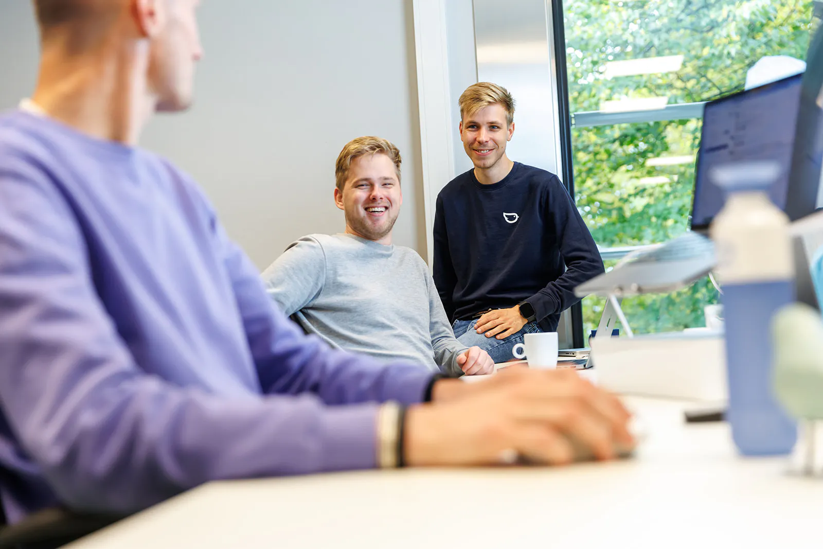 Drie collega'a op de werkvloer lachen naar de camera