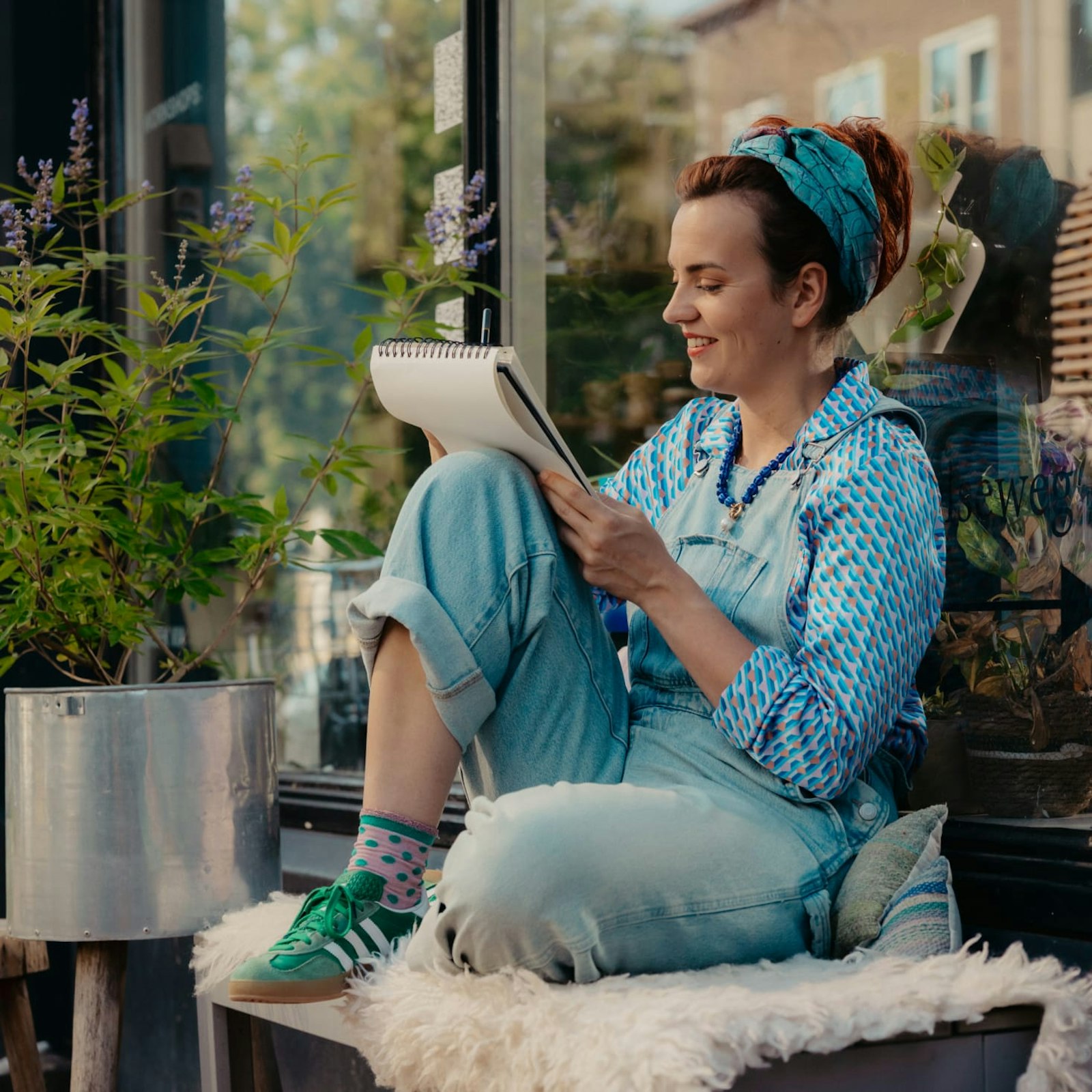 Merel met schetsblok zittend op een bankje voor haar winkel