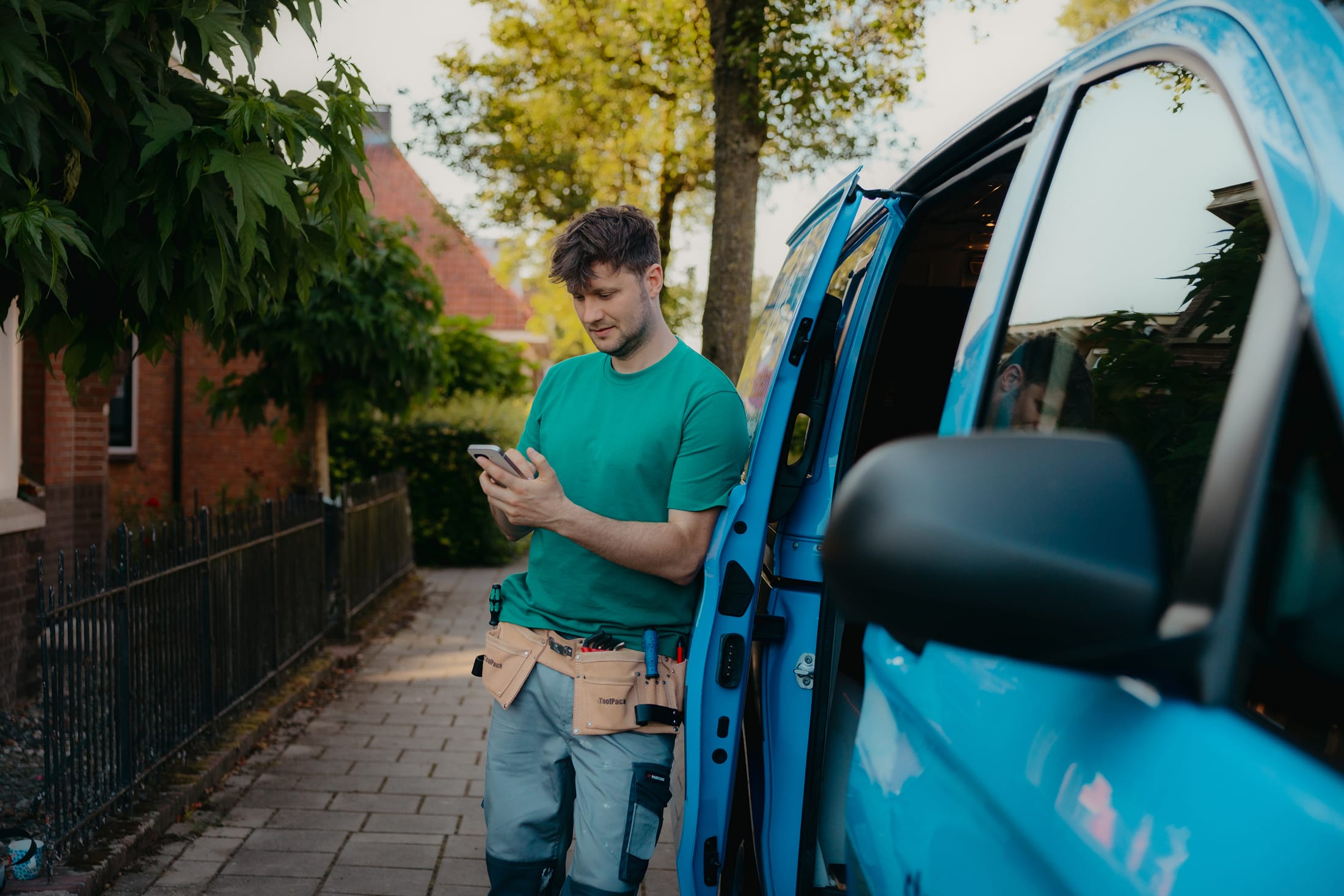 Arend leunt tegen zijn bus en kijkt op zijn mobiel