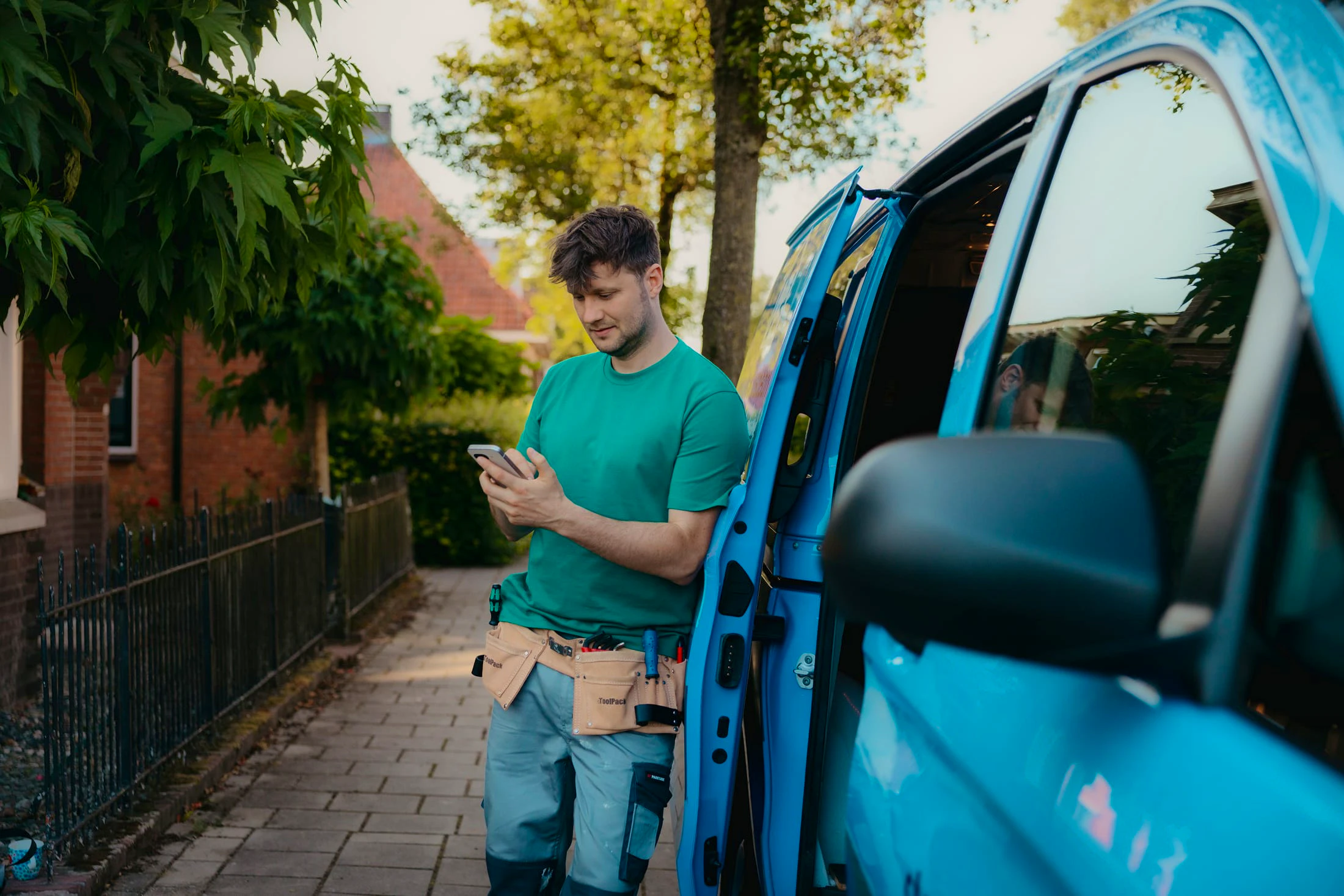 Arend leunt tegen zijn bus en kijkt op zijn mobiel