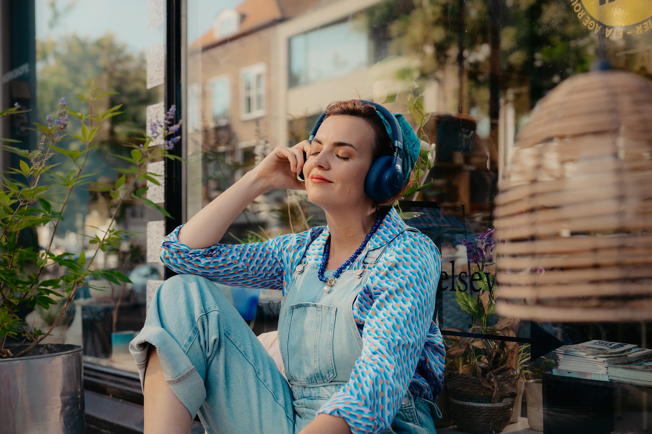Merel met headphones buiten op een bankje voor haar winkel
