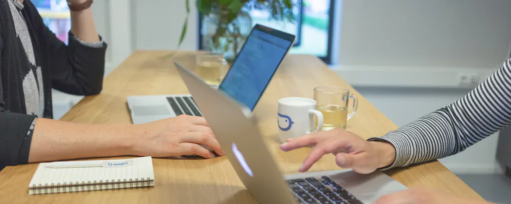 Collega's met handen en kopjes bij laptop met notitieblok