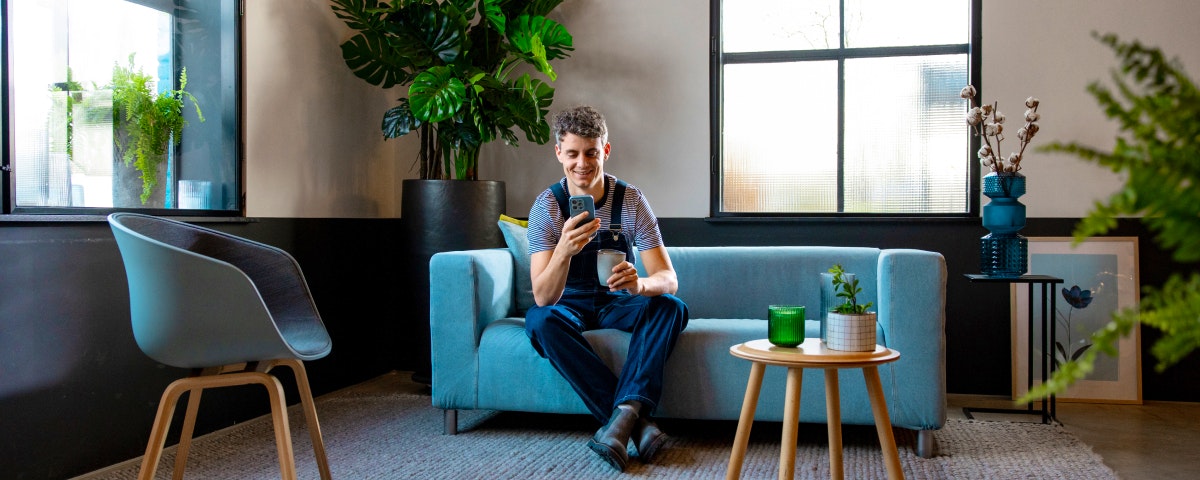 Ondernemer zit op een blauwe bank met een kop koffie en zijn telefoon. 