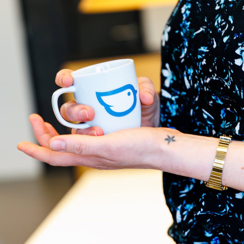 Handen van collega met kopje koffie met Moneybird logo