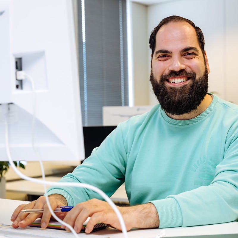 Soner achter zijn desktop terwijl hij lachend in de camera kijkt