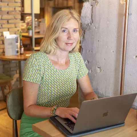 Annamarie kijkt in de camera en werkt achter haar laptop