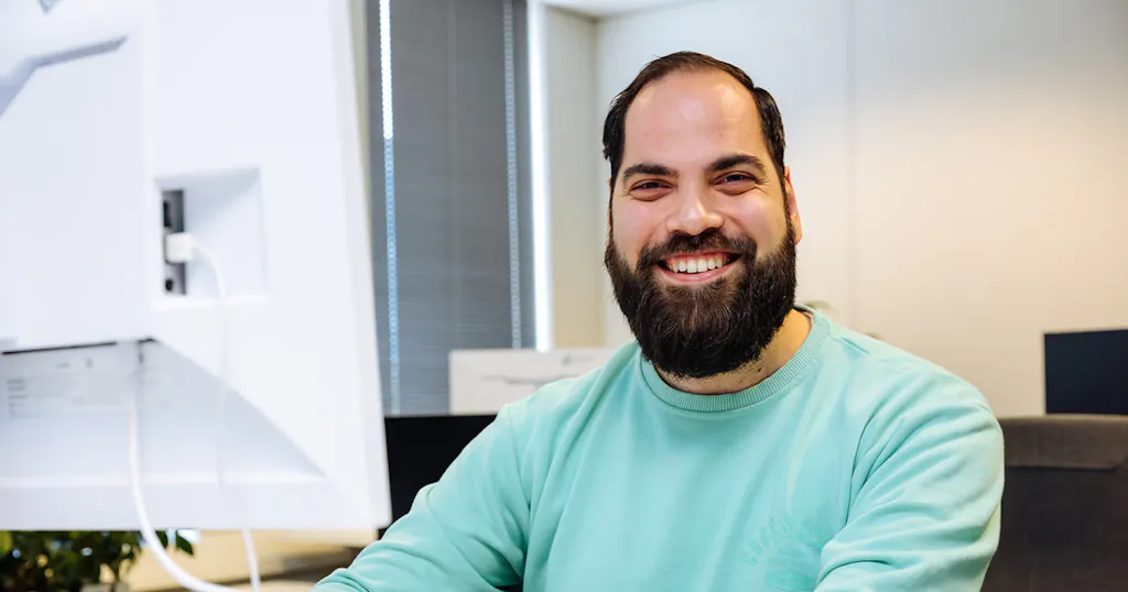 Soner lachend achter zijn beeldscherm op kantoor