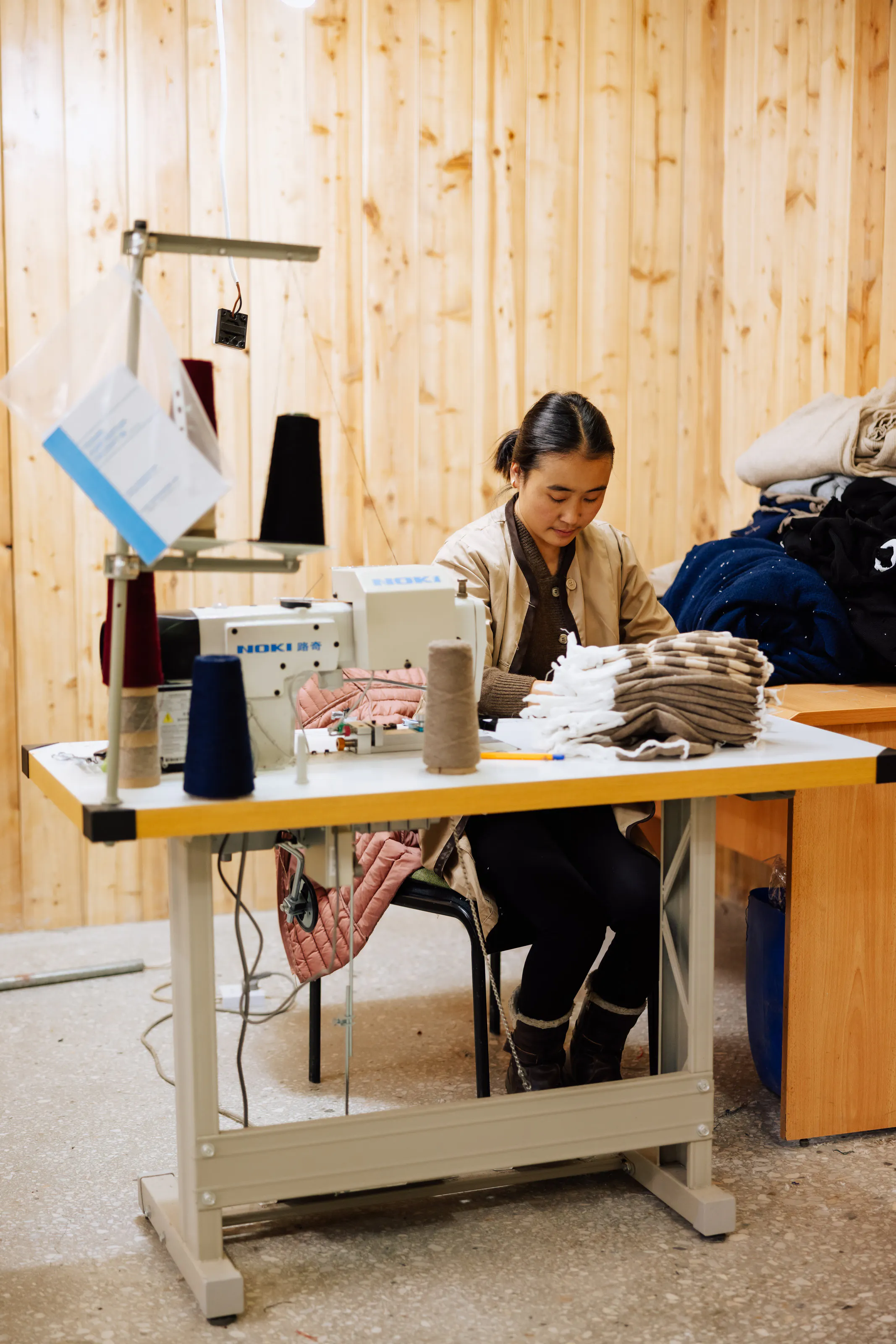 An employee sewing beside stacks of knitted pieces.