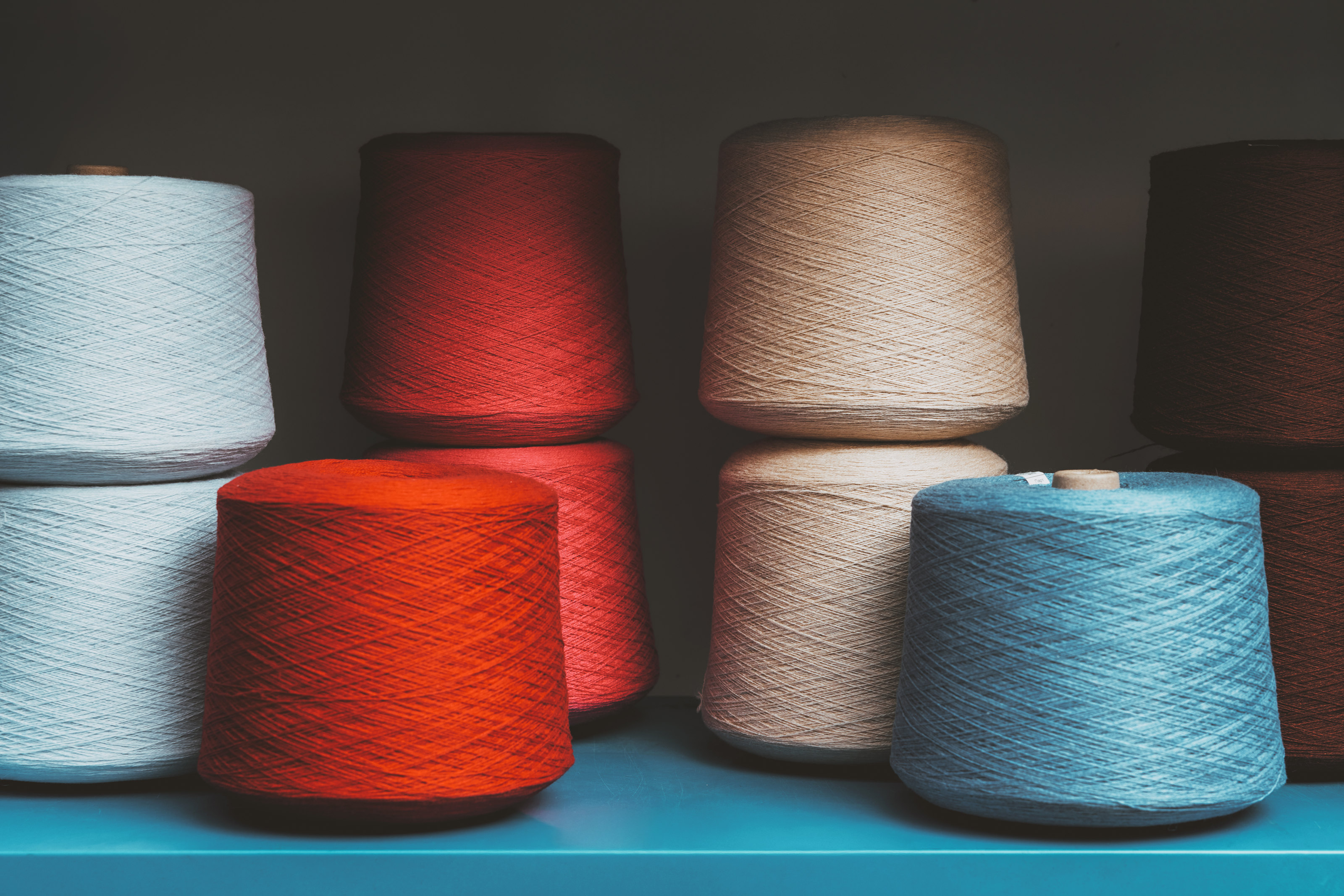 Coloured yarn cones arranged on a shelf.