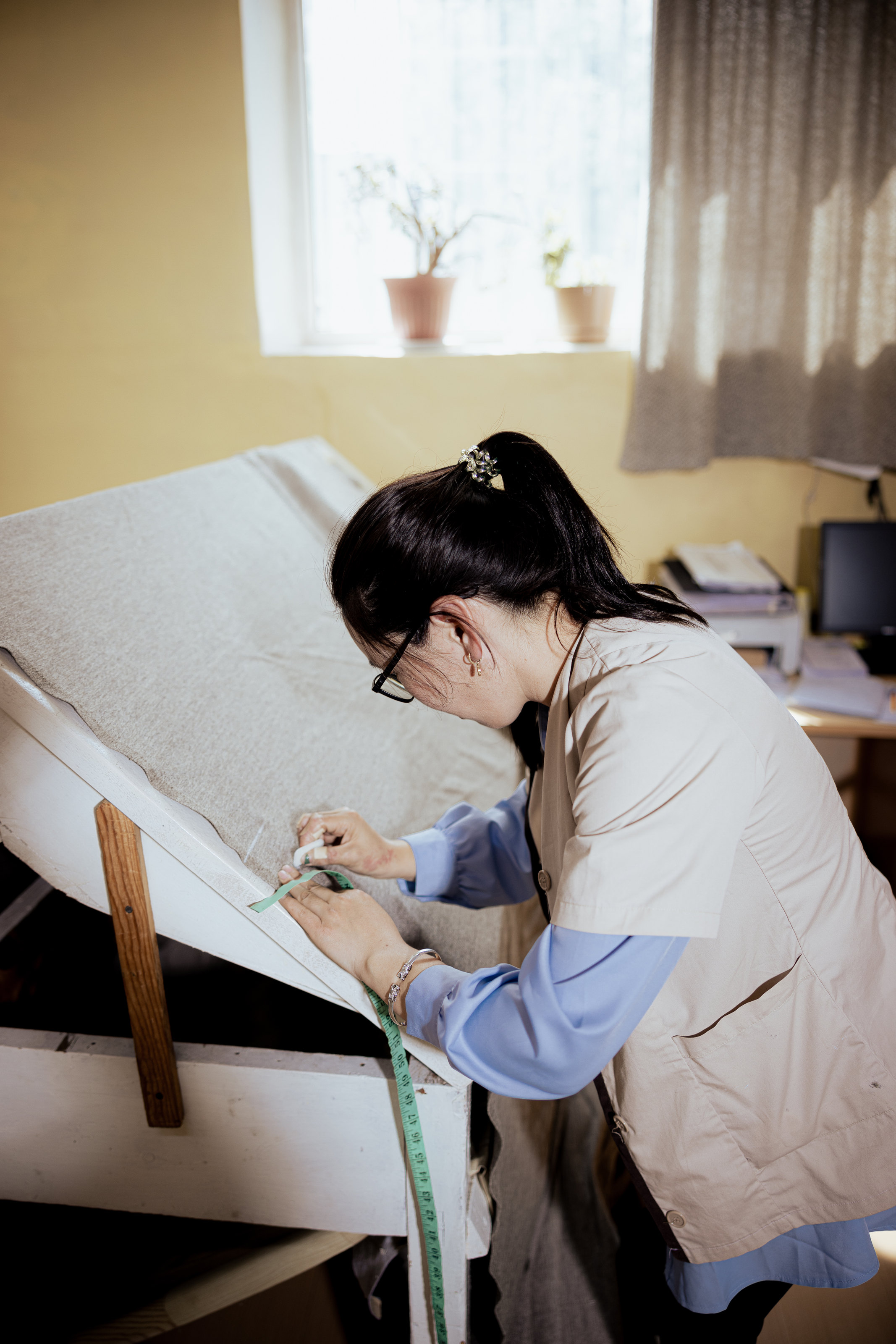 A person examining a light-coloured textile on an angled table.