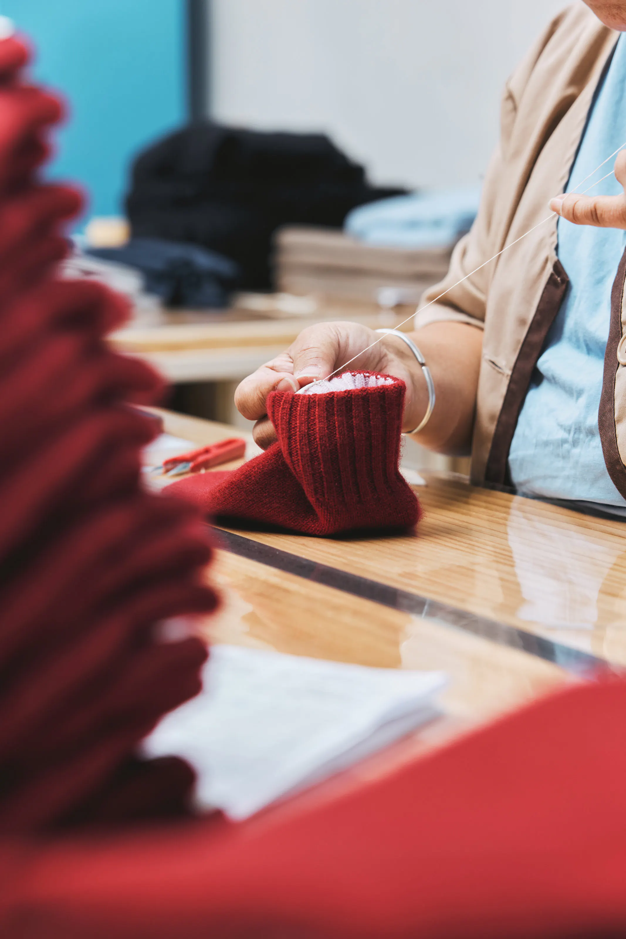 Hands holding a red knitted cuff at a worktable.