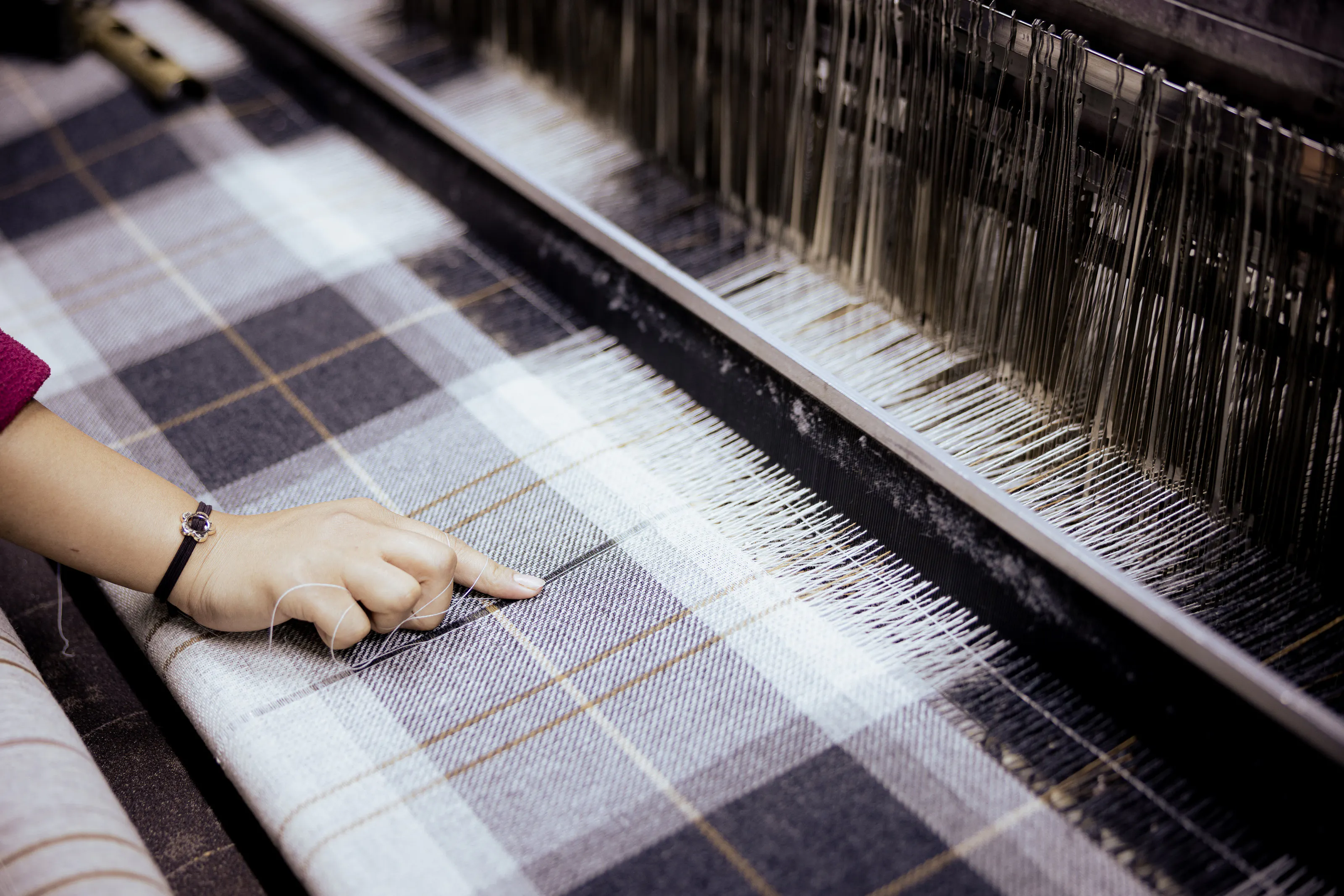 A hand beside checked textile on a loom.