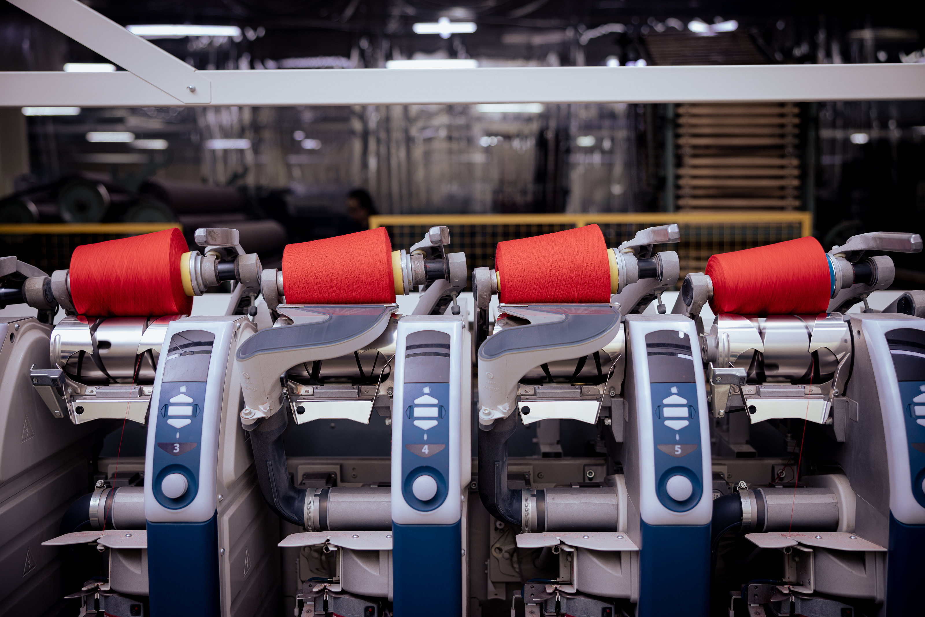 Red yarn packages mounted on textile machines.