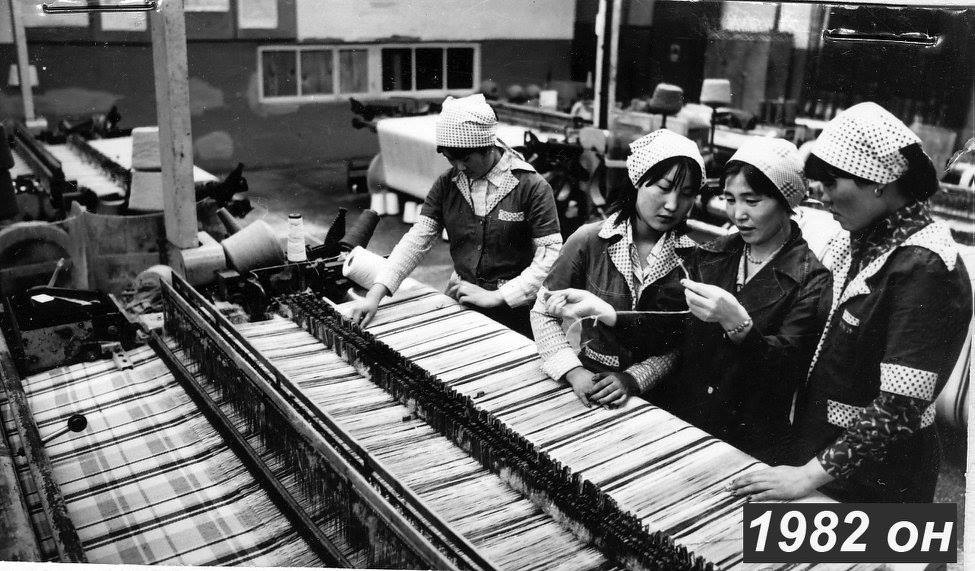 Black-and-white archive photograph of people beside textile machinery.
