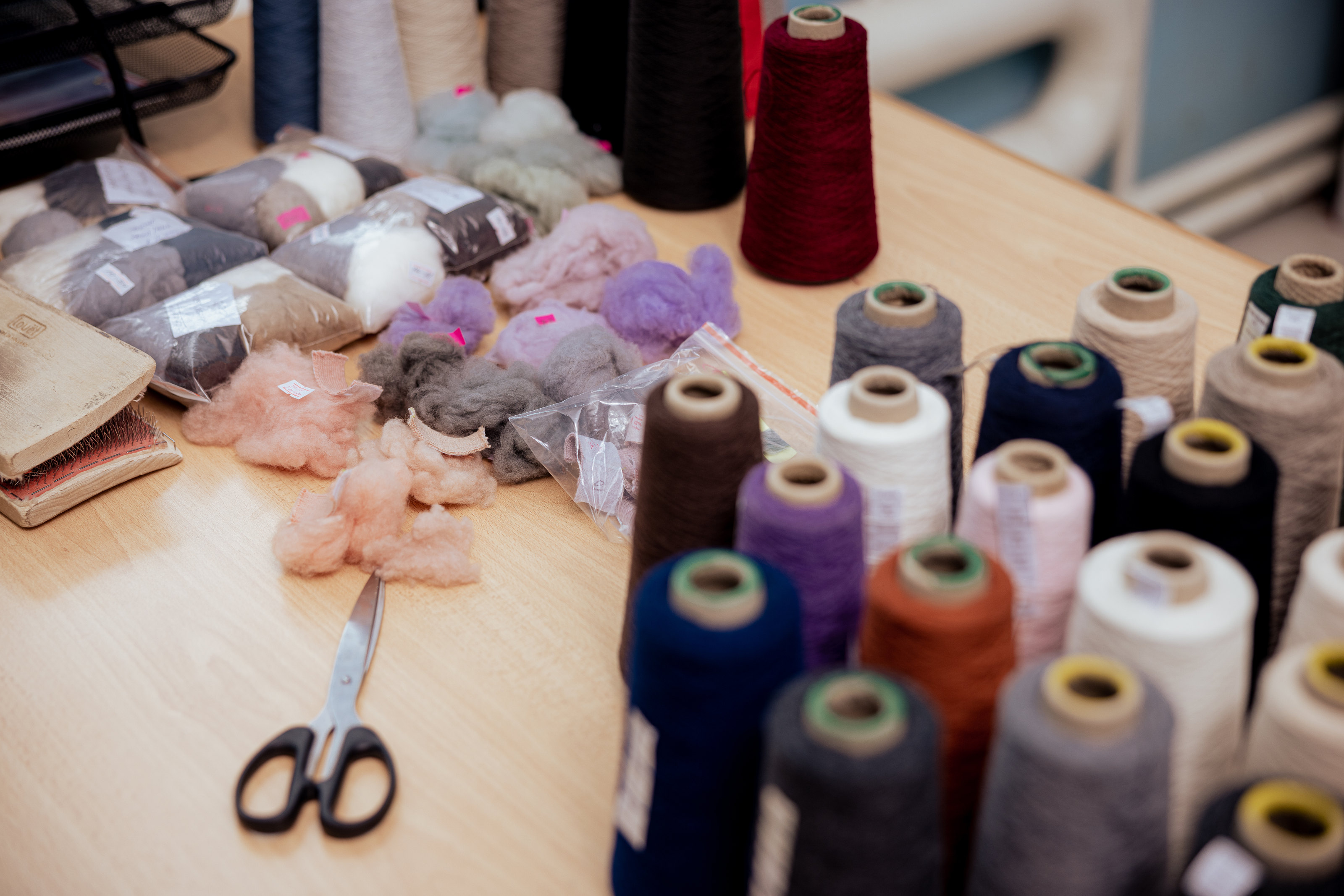 Yarn cones, loose fibre and scissors on a worktable.