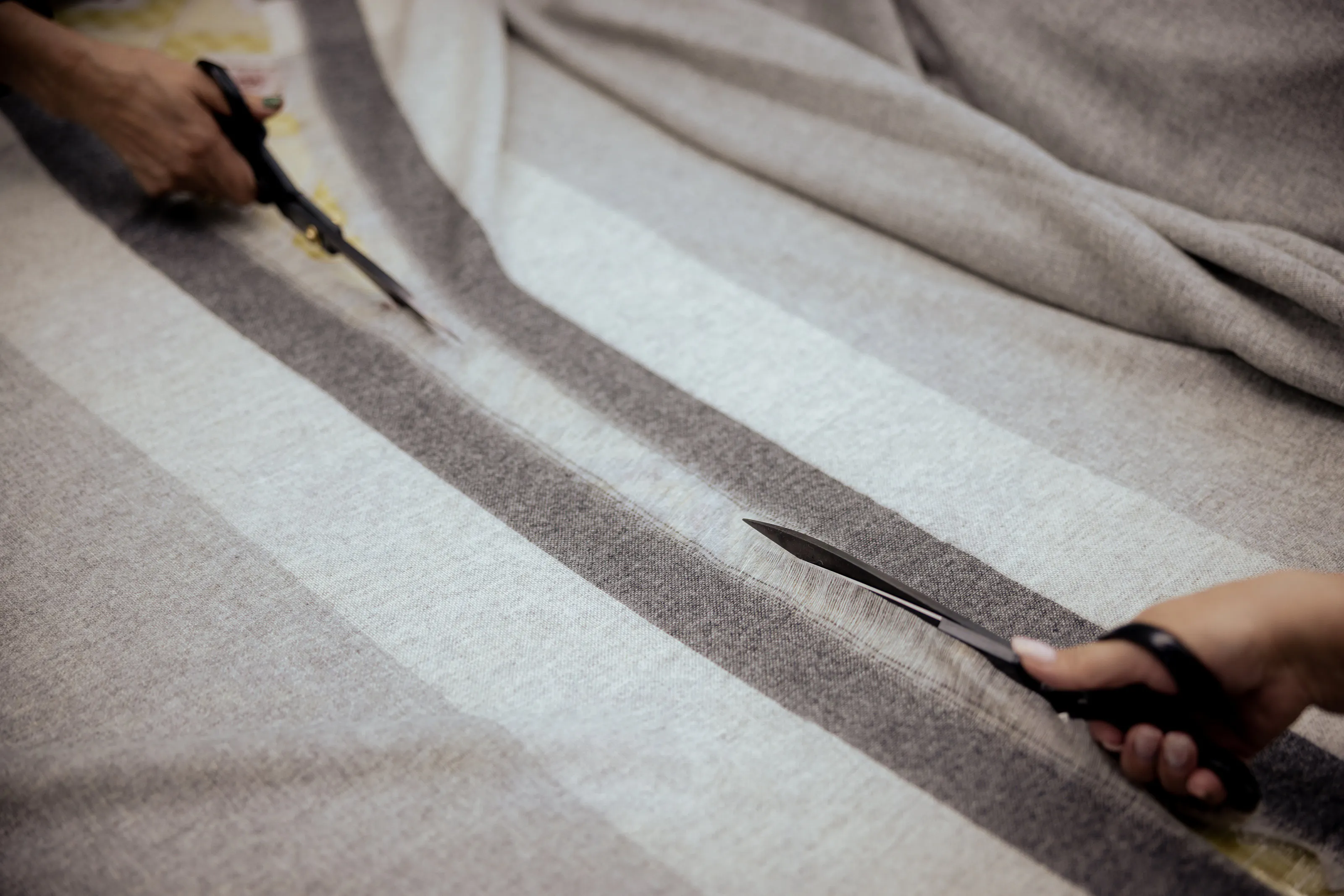 Hands cutting along the edge of a textile.