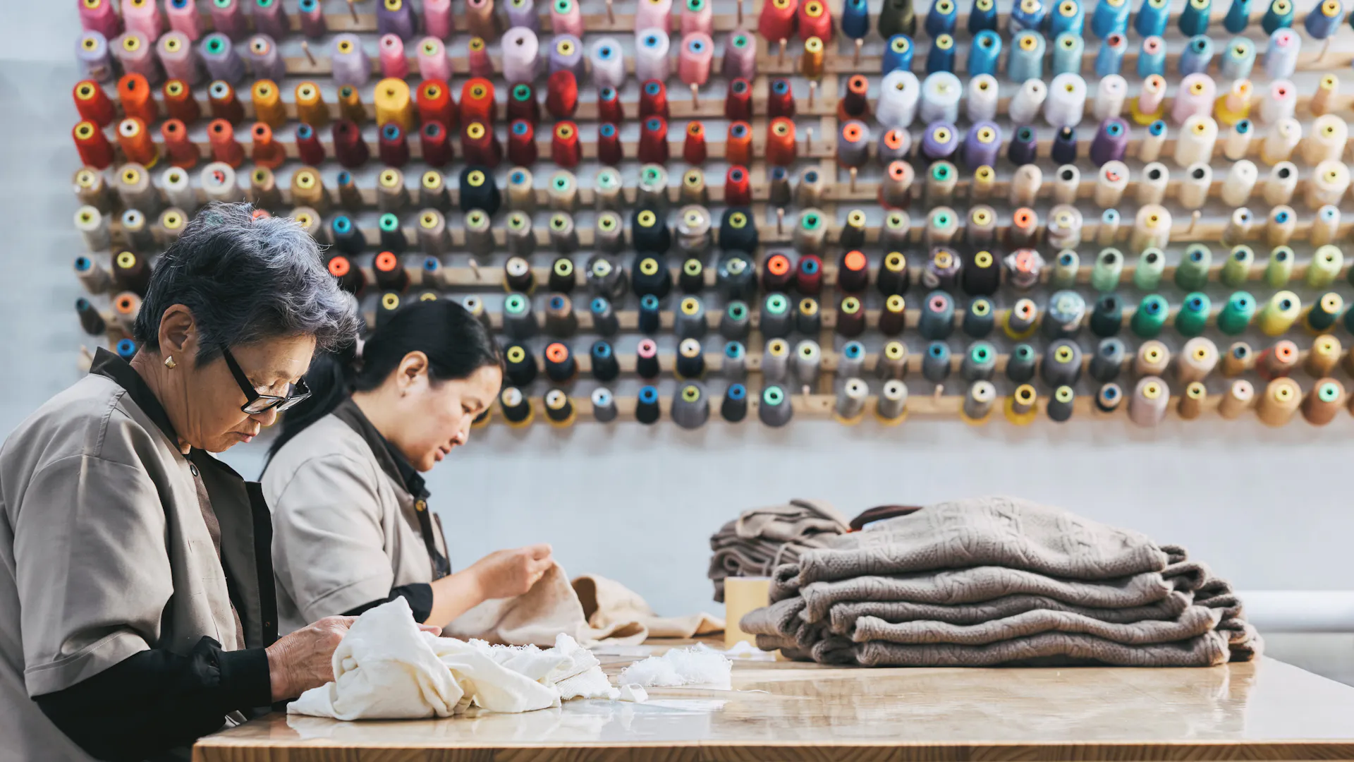 Employees working beside a wall of coloured thread.