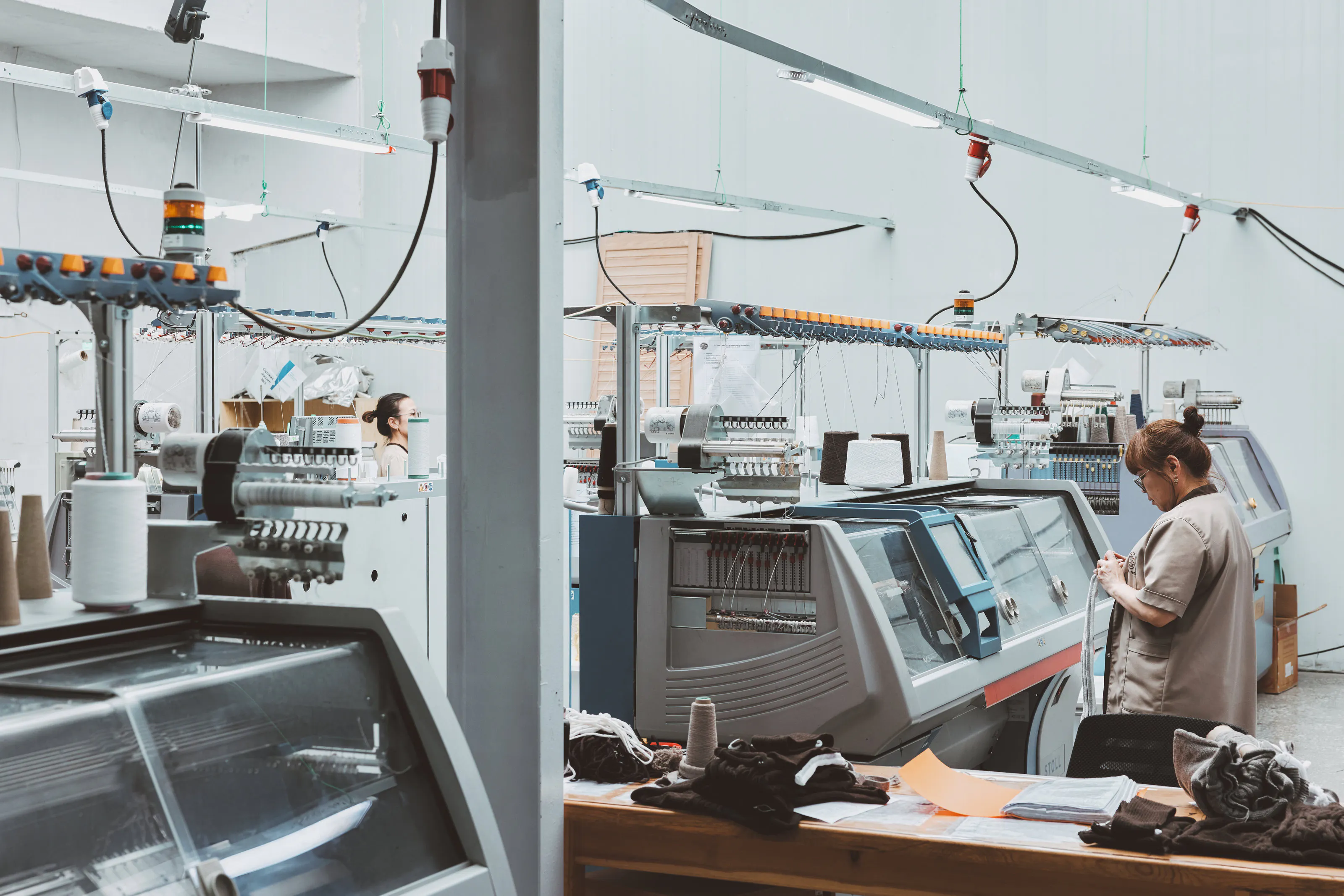 A row of flat knitting machines with an operator.