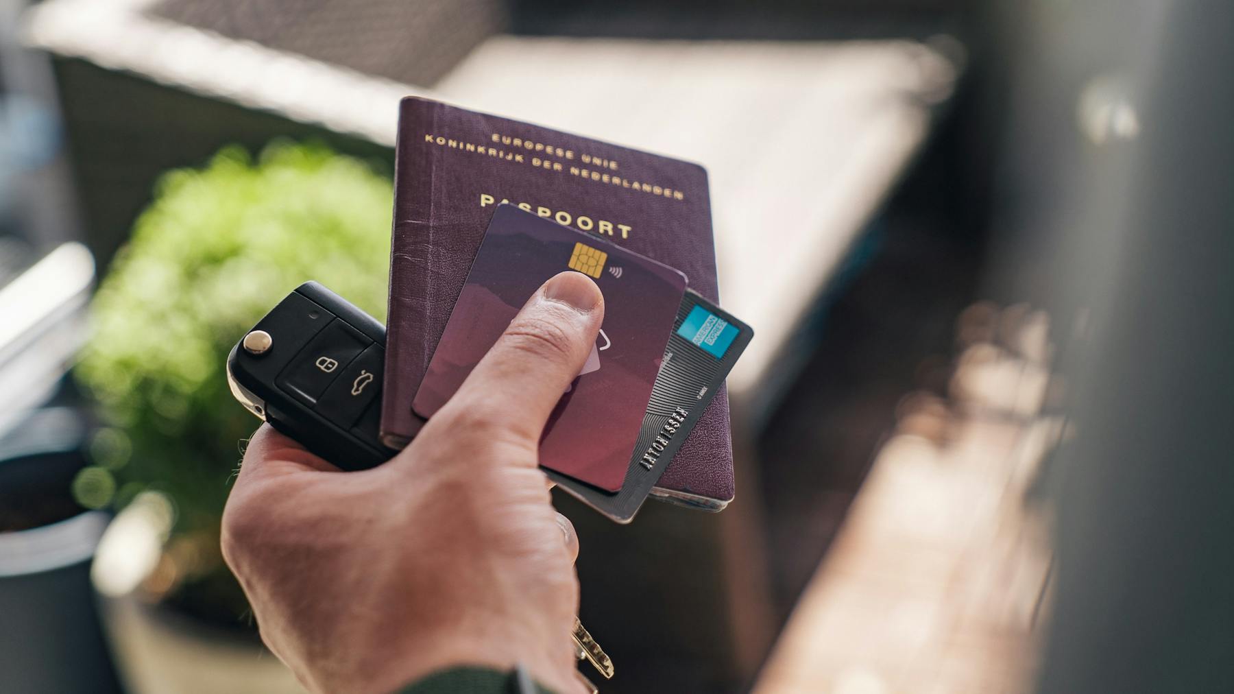A man's hand holding cards, car keys, and a passport