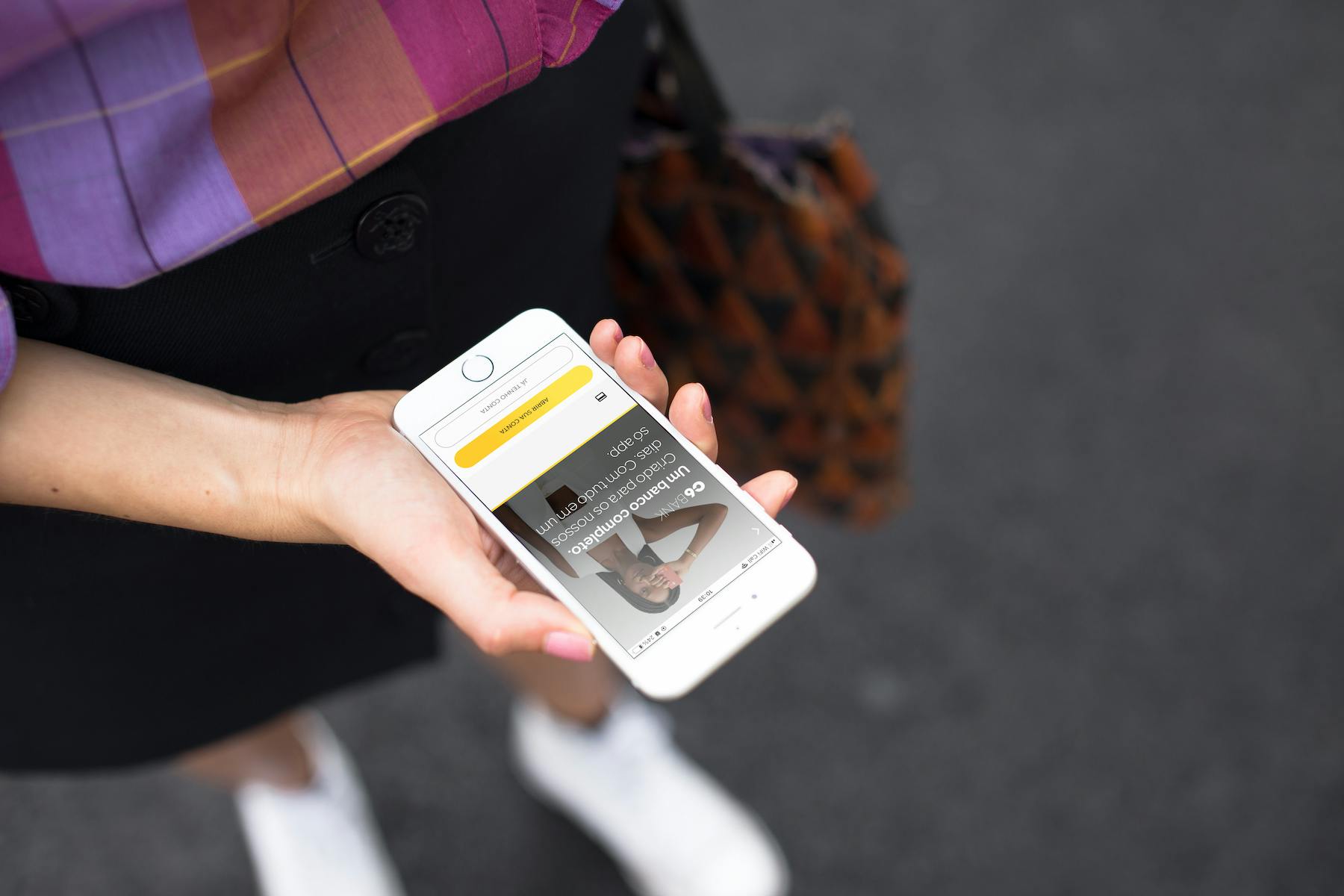 Mulher segura um iPhone branco na mão e acessa sua conta no app do C6 Bank