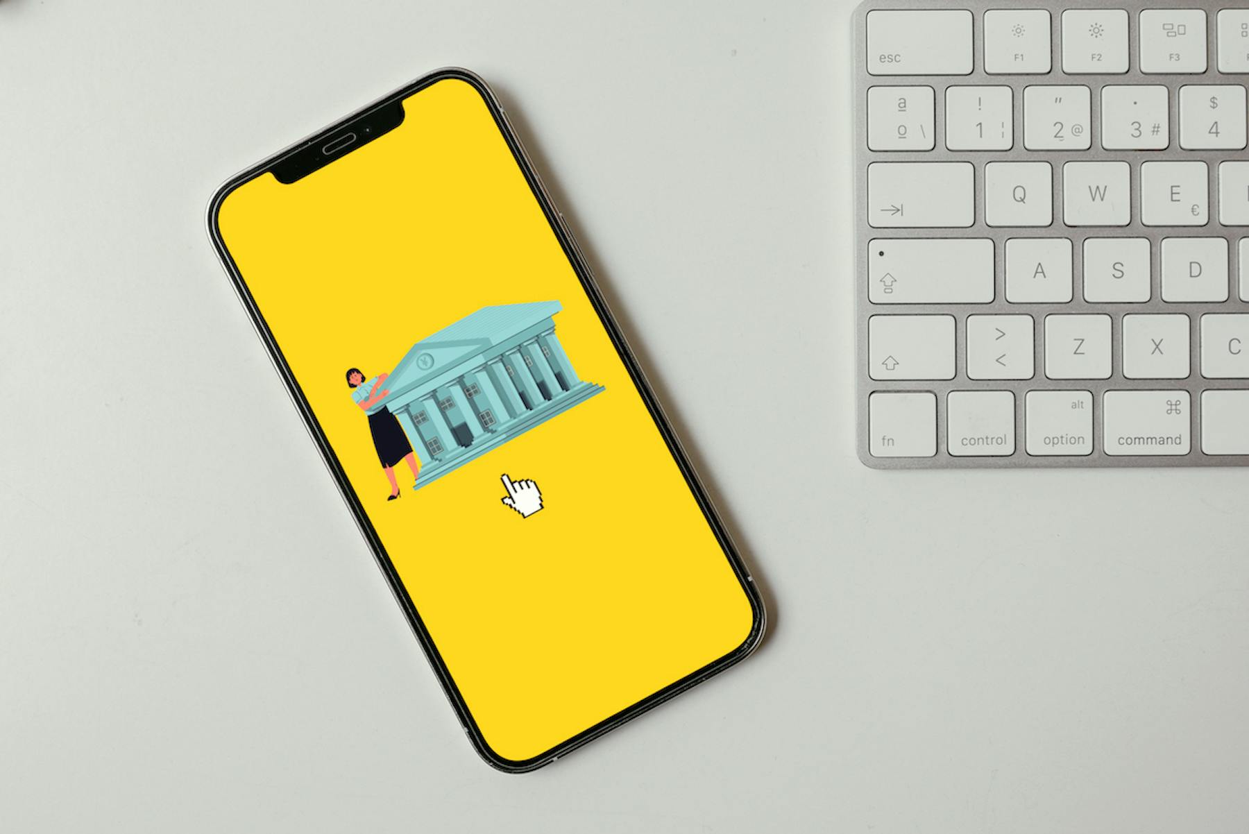 Smartphone mostra a ilustração de um banco digital com fundo amarelo e um teclado ao lado na mesa