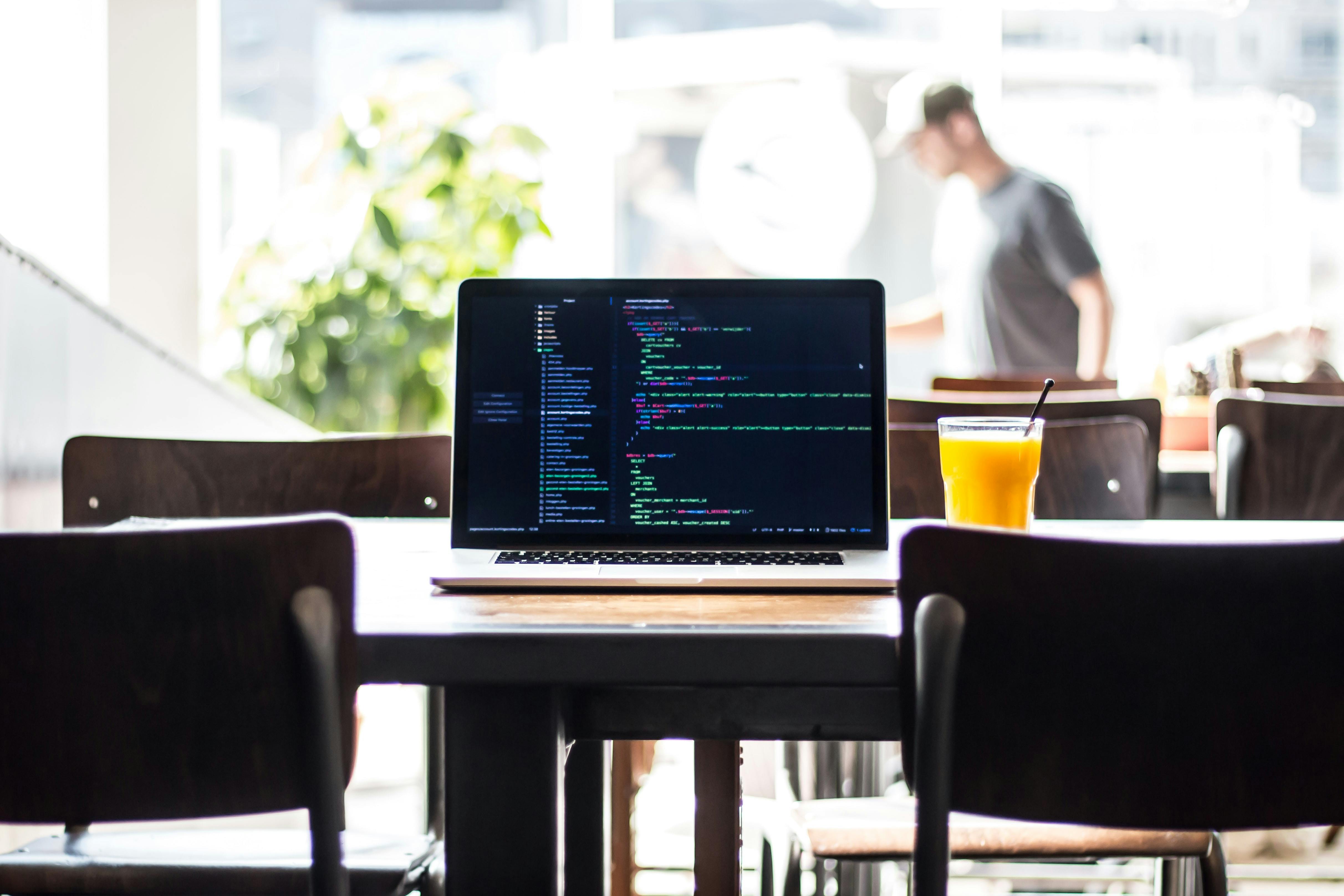 A computer and orange juice on a table with a man in the background