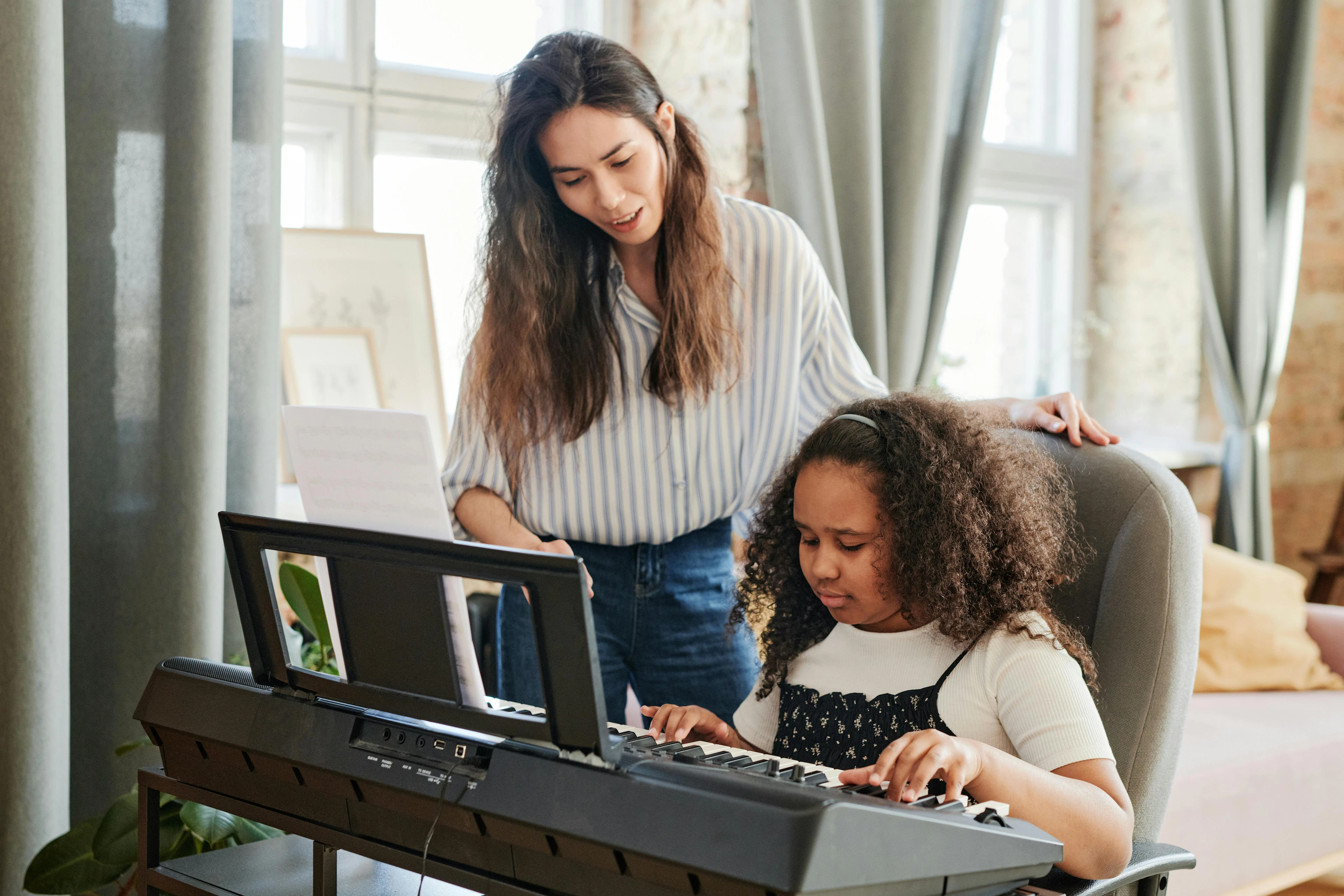 A young girl playing the piano with her teacher guiding and encouraging her, highlighting a supportive music lesson environment.