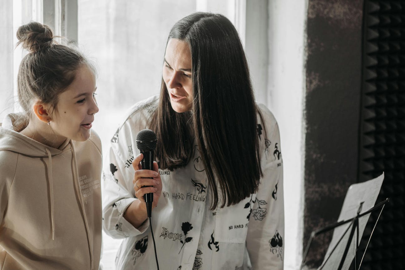 A music teacher and a young student singing together during a lesson to help the student prepare for auditions. The teacher is holding a microphone and encouraging the student, creating a warm and supportive atmosphere