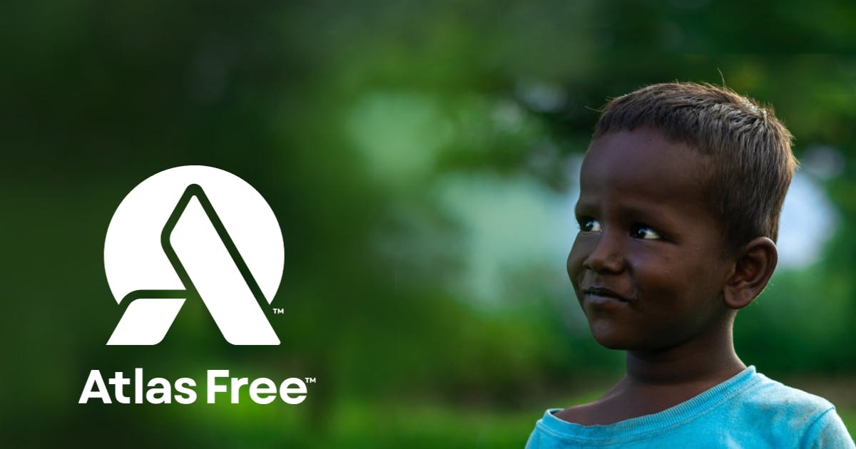 A young child is looking towards the Atlas Free Logo with blurry green trees in the background.