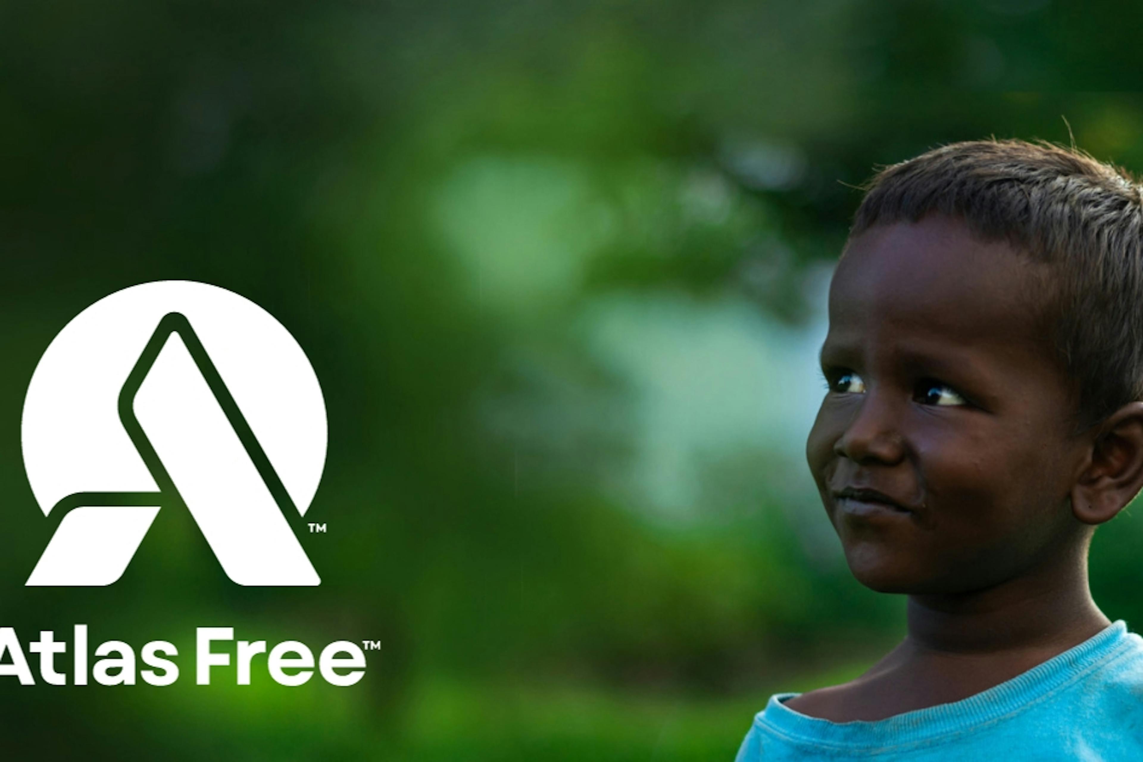A young child is looking towards the Atlas Free Logo with blurry green trees in the background.