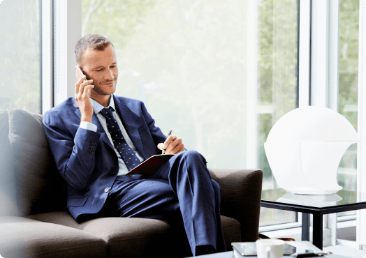 A man in work attire speaks on the phone whilst sitting on a sofa