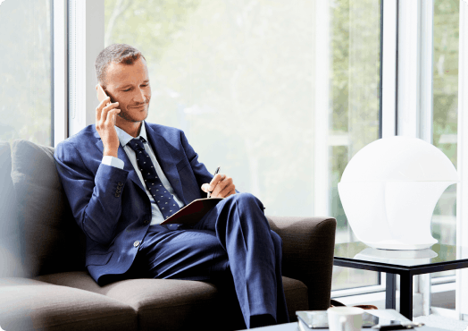 A man in work attire talking to the phone whilst sitting on a sofa