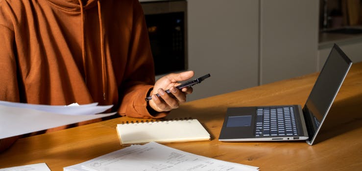 A hand holding a phone in front of a laptop